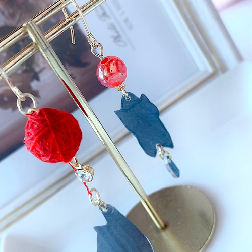 ぷらぷら揺れる毛糸玉で遊ぶ黒猫と首ねっこをつままれる黒猫のピアス  