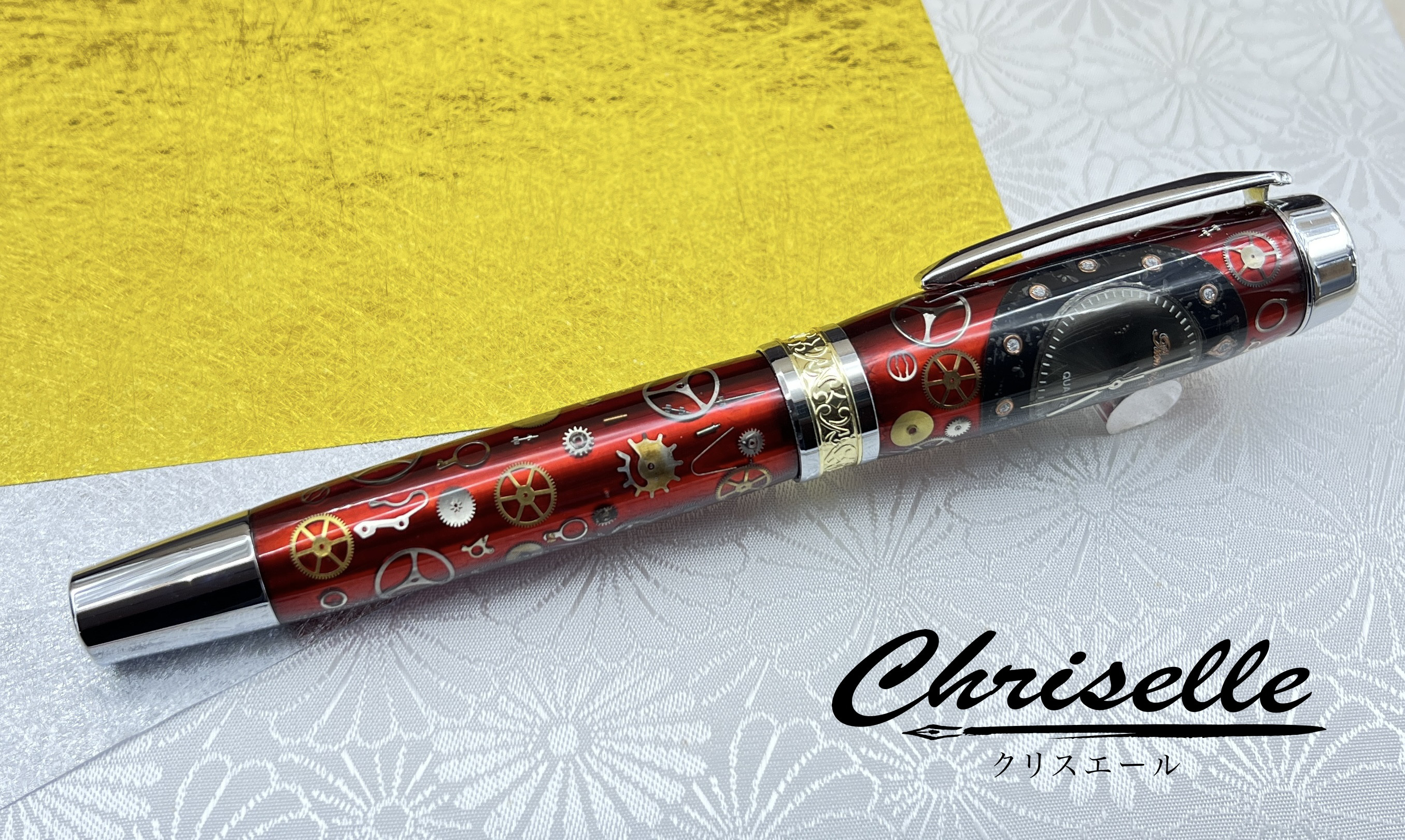 メタルっぽい赤樹脂の上に腕時計のゼンマイ・ネジ・文字盤を乗せたボールペン