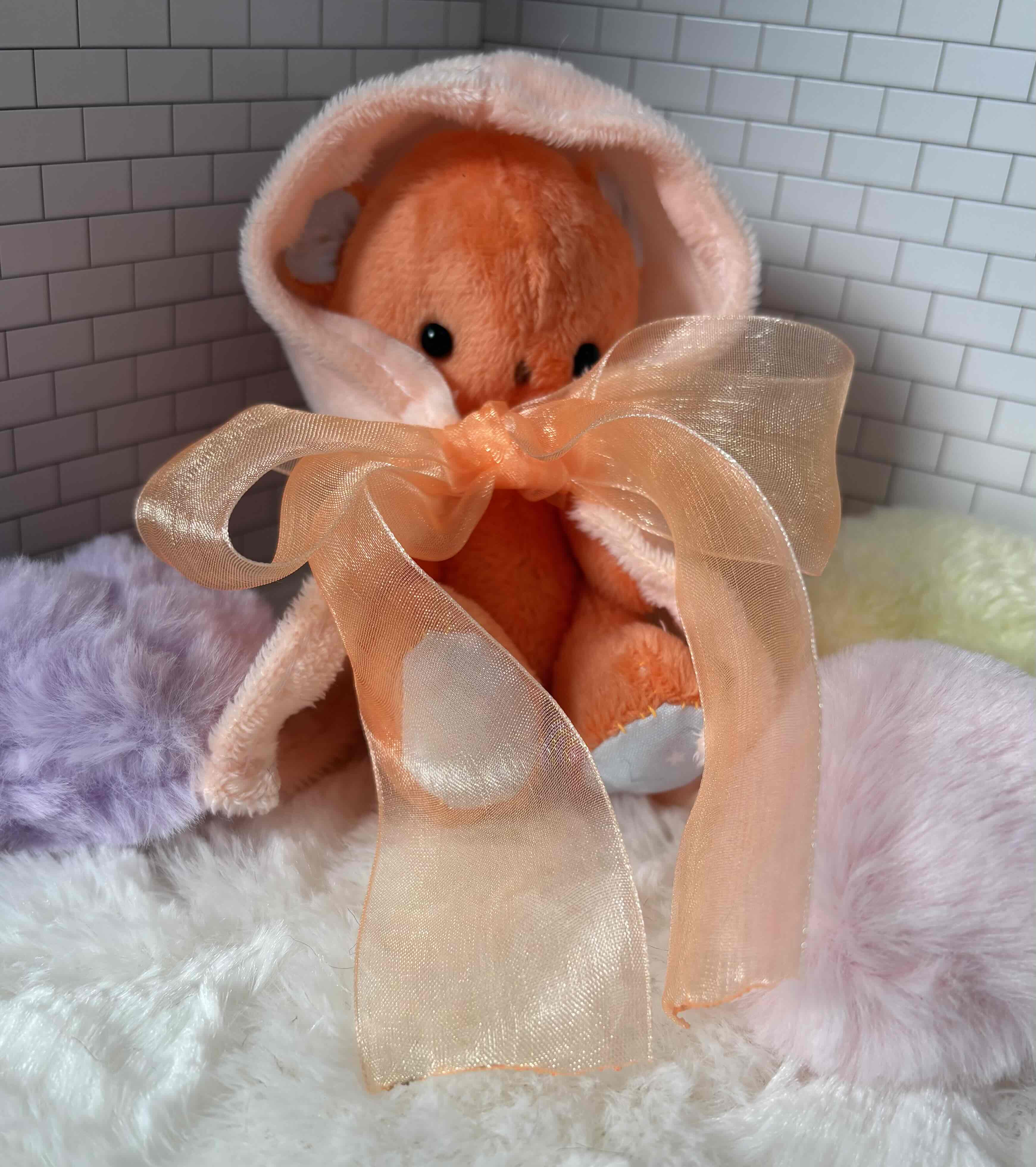 フード付きマントを着たオレンジのくまさんのぬいぐるみ